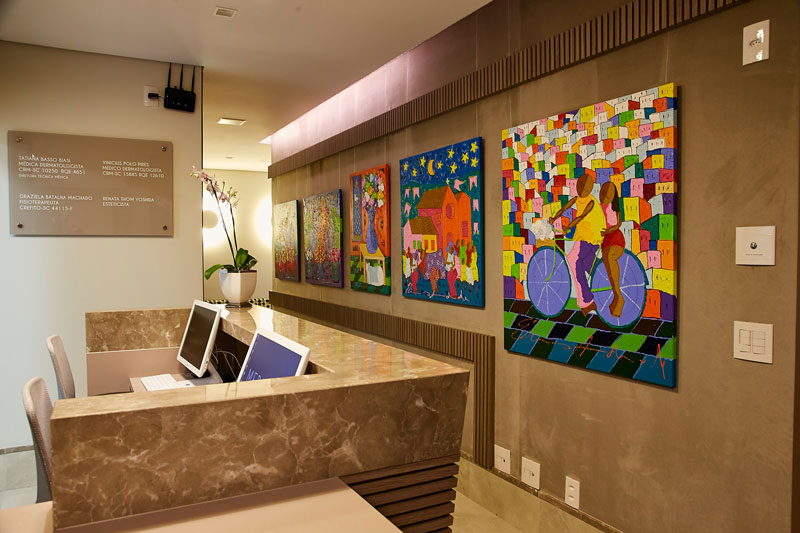 Recepção de clínica de dermatologistas em Florianópolis em mármore com dois computadores, ao fundo parede decorada com quadros coloridos de estilo moderno.