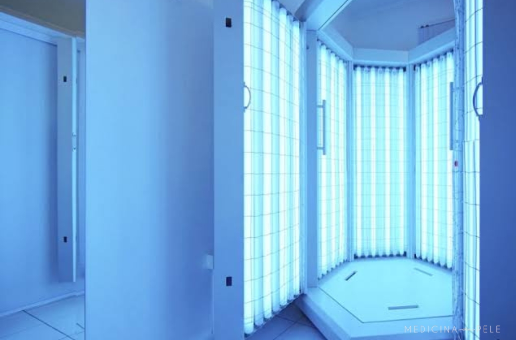 Fotografia mostra cabine vertical equipada com lâmpadas de luz ultravioleta azuladas, utilizada em sessões de fototerapia para tratamento de doenças de pele como psoríase, vitiligo e dermatite.