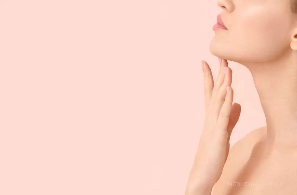 Fotografia mostra uma mulher com pele lisa tocando suavemente a região inferior do rosto e do pescoço, sugerindo cuidados estéticos com foco em definição do contorno facial, como o uso de enzimas lipolíticas ou esvaziador injetável.