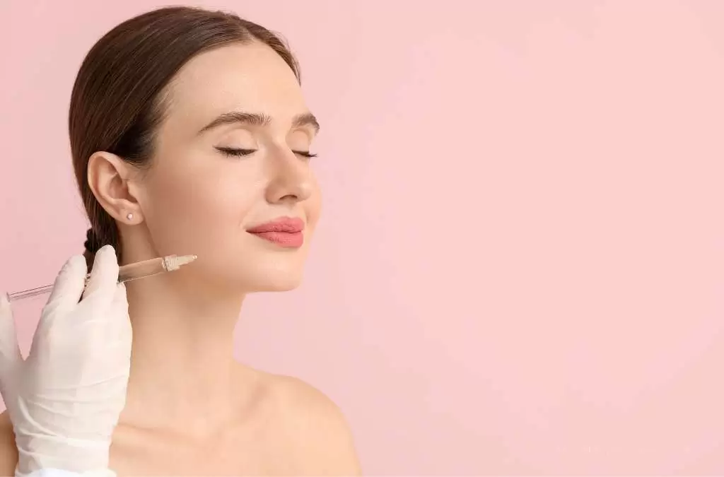 Fotografia mostra uma mulher com expressão relaxada e olhos fechados enquanto profissional aplica injeção próxima à mandíbula, ilustrando procedimento de intradermoterapia facial.