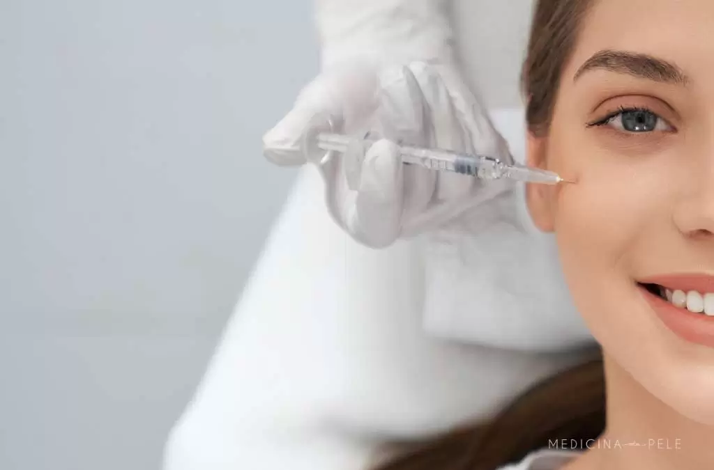Fotografia mostra uma mulher sorrindo enquanto recebe uma aplicação de injeção próxima aos olhos por profissional com luvas, ilustrando tratamento estético com skinbooster para hidratação profunda da pele.